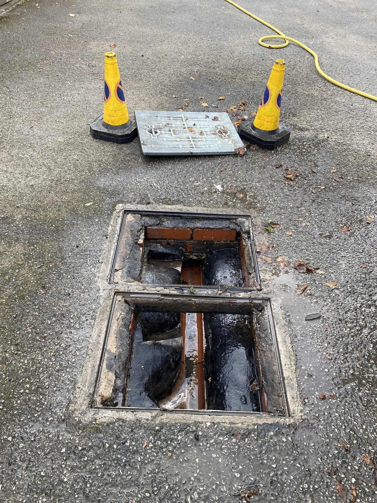 Open manhole with blocked drain and standing water